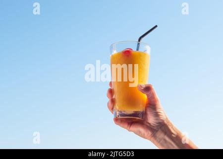 Woman`s hand raising glass with refreshing orange cocktail in the air. Stock Photo